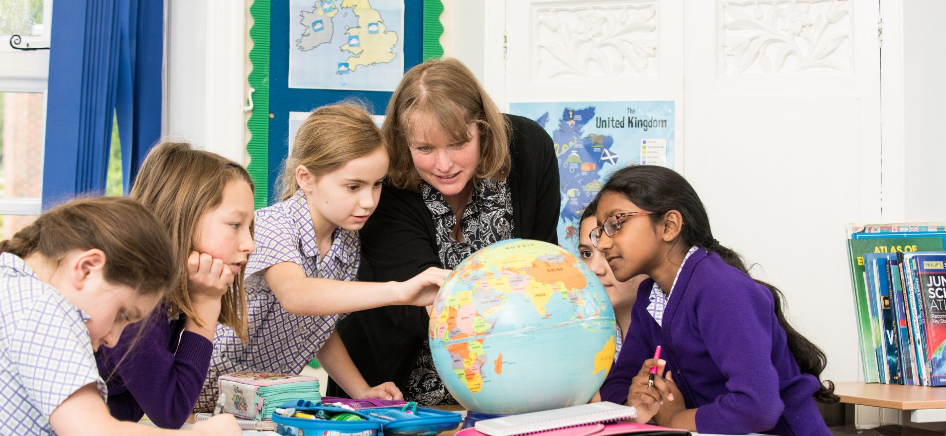 school girls looking at a globe with teacher
