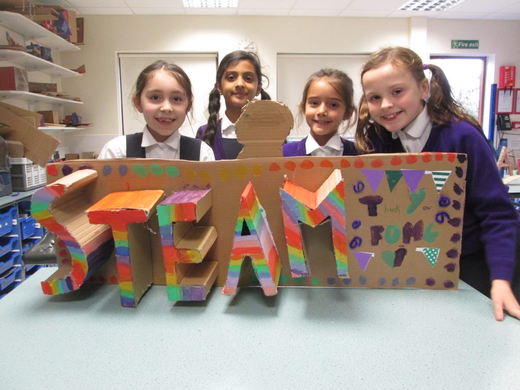Children with a cardboard cut out that reads "STEAM"